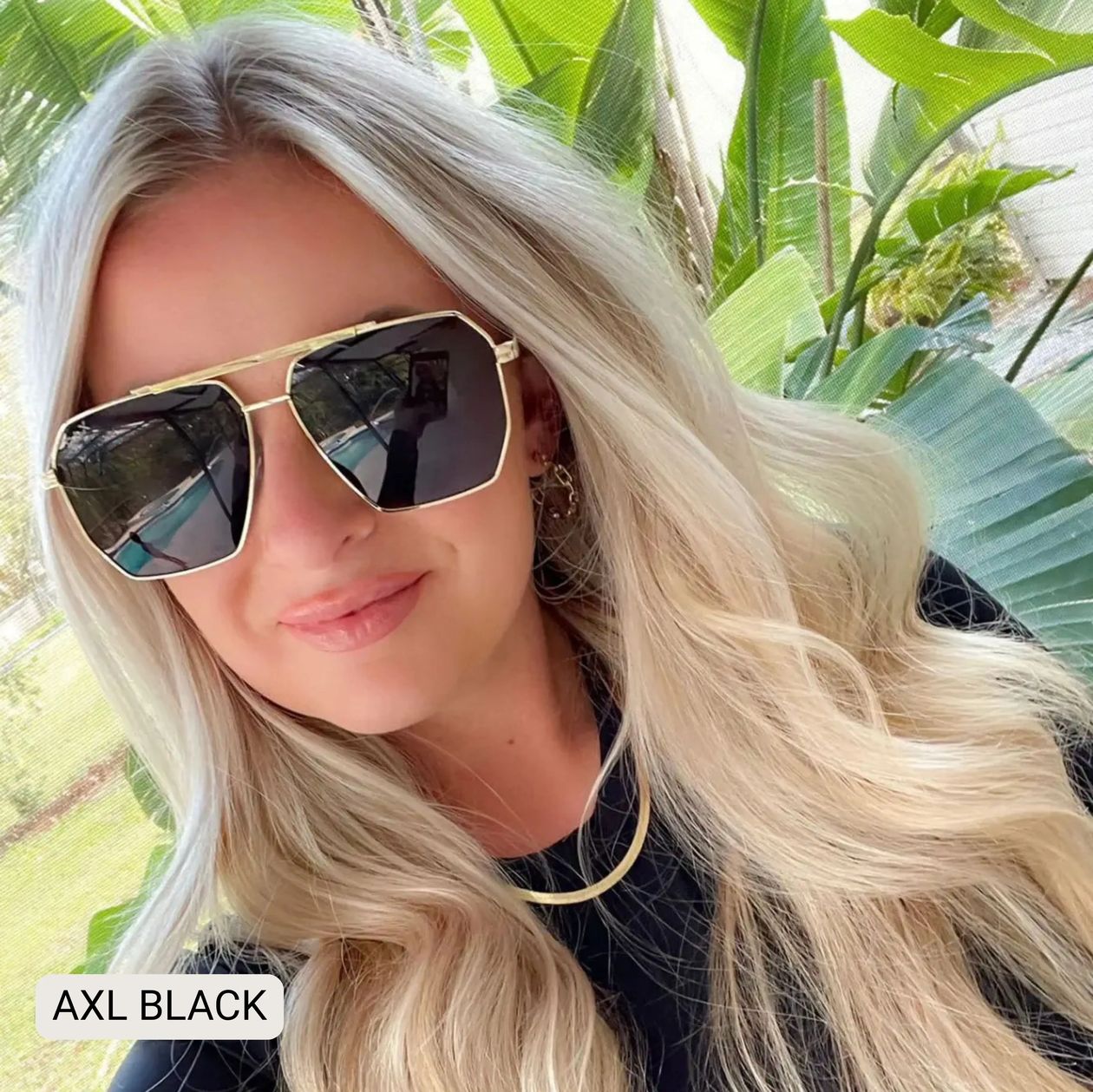 Woman wearing gold-framed sunglasses with a tropical background