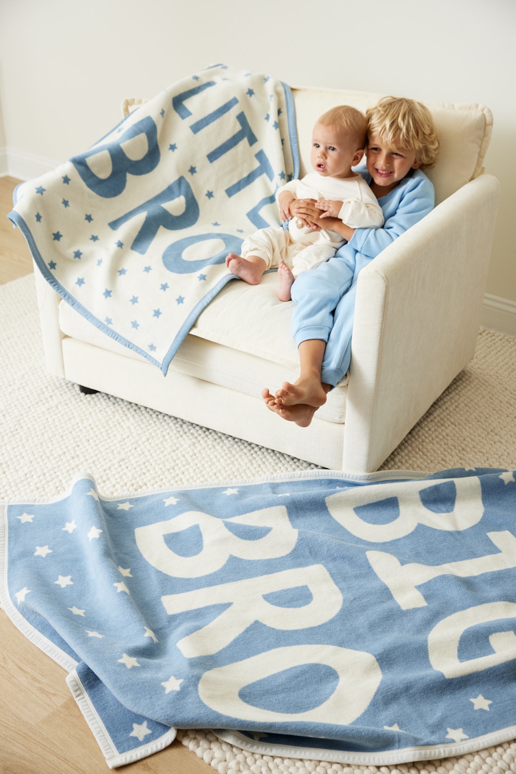 Siblings playing with the Chappywrap Big Bro blanket on a sofa