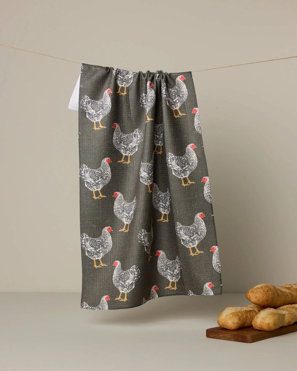 Towel with chicken pattern hanging on a line against a beige background