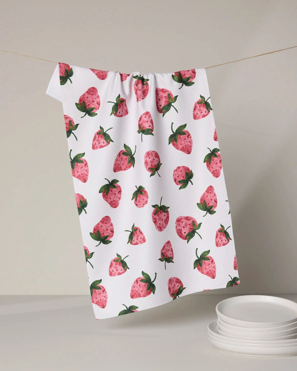 Towel with strawberry pattern hanging on a line against a neutral background