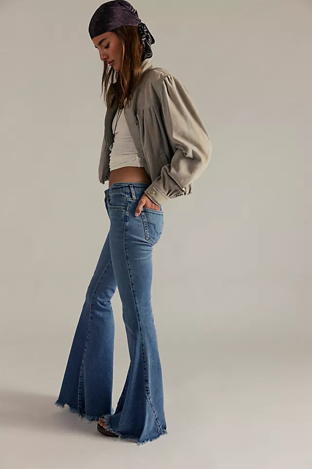 Woman wearing a beige jacket, white crop top, and blue flared jeans on a plain background