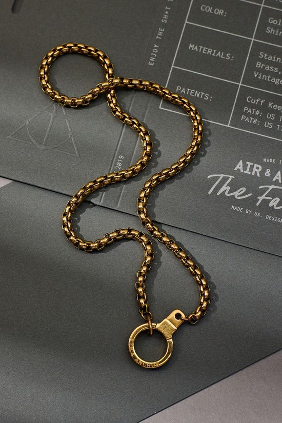 Gold chain necklace on a gray surface with a branded paper underneath