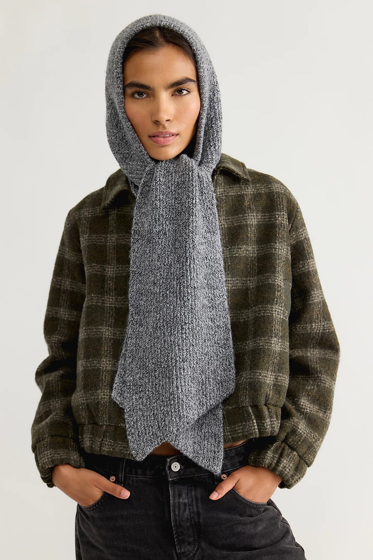 Model wearing the Free People Extra Large Balabonnet in grey, an oversized ribbed knit hood with long scarf ties, over a green plaid jacket