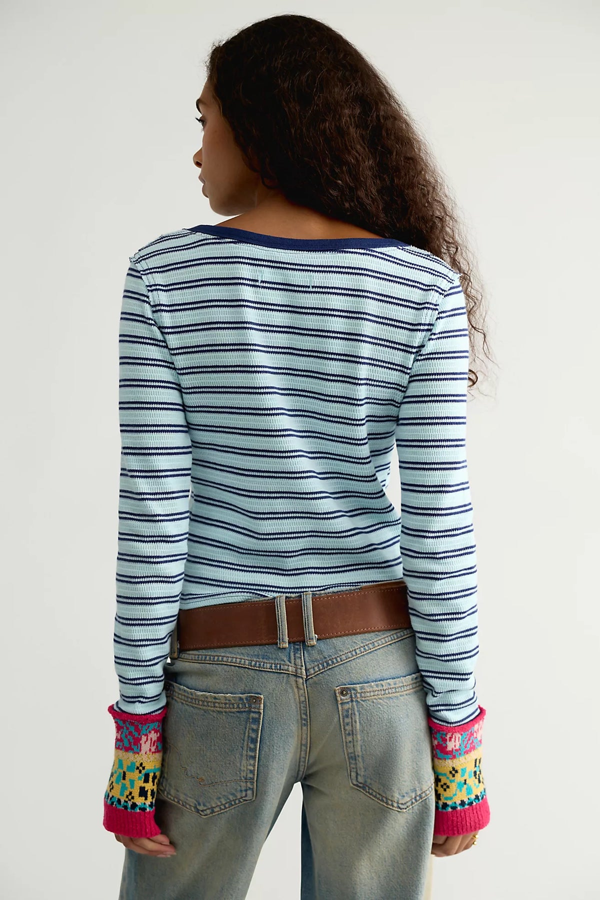 Back view of the Free People Noa Cardi, a fitted blue and navy striped cardigan with pink multicolor embroidered cuffs, worn with light wash jeans and a brown belt