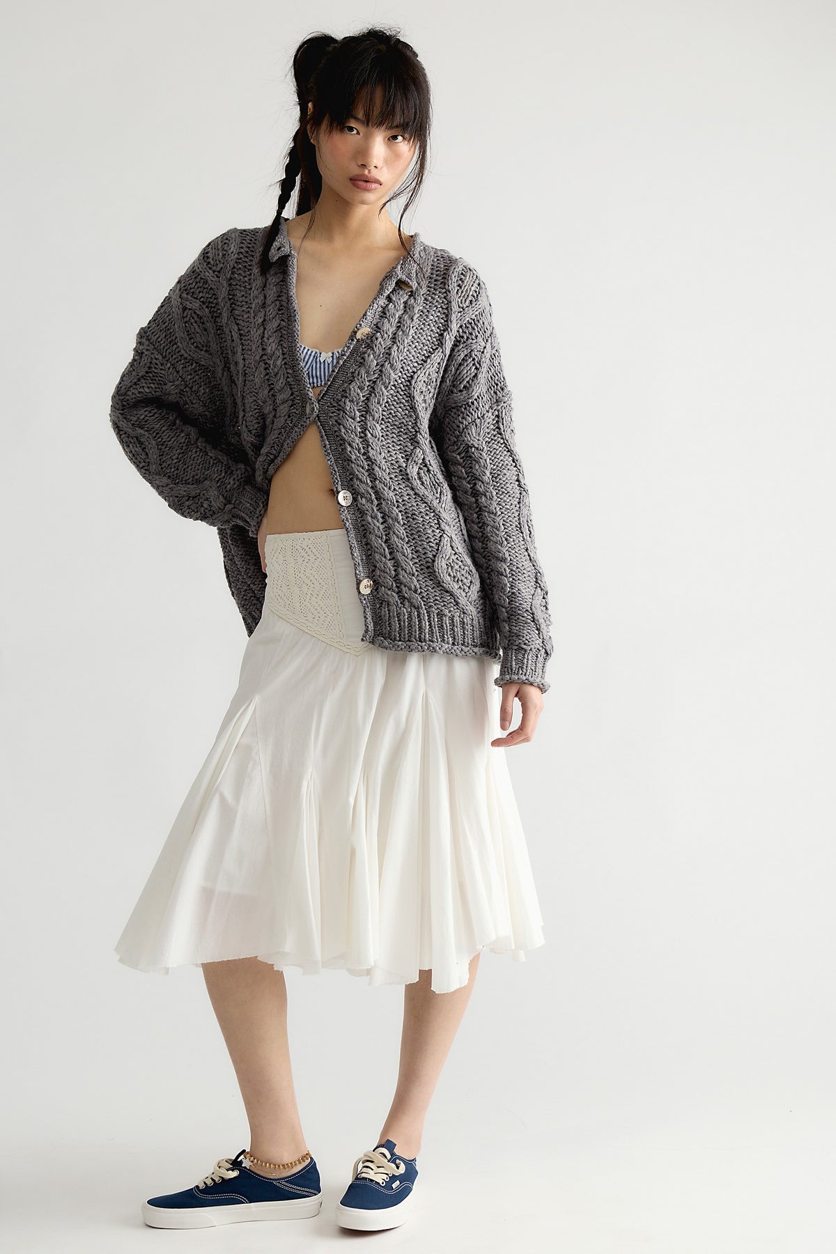 Model wearing the Free People Opal Cable Knit Cardigan in Steel Grey with a white skirt, full-length front view