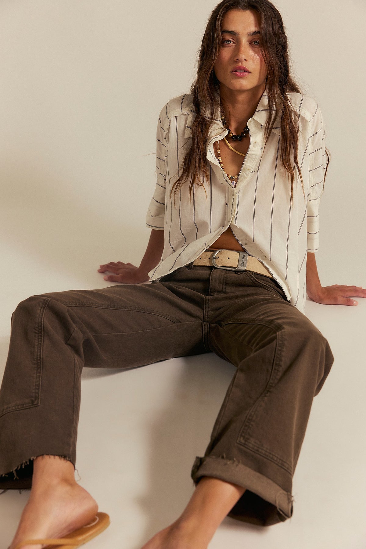 Model seated in the Seaside Cotton Stripe Shirt in Ivory Combo with brown trousers, showing the balloon dolman sleeves