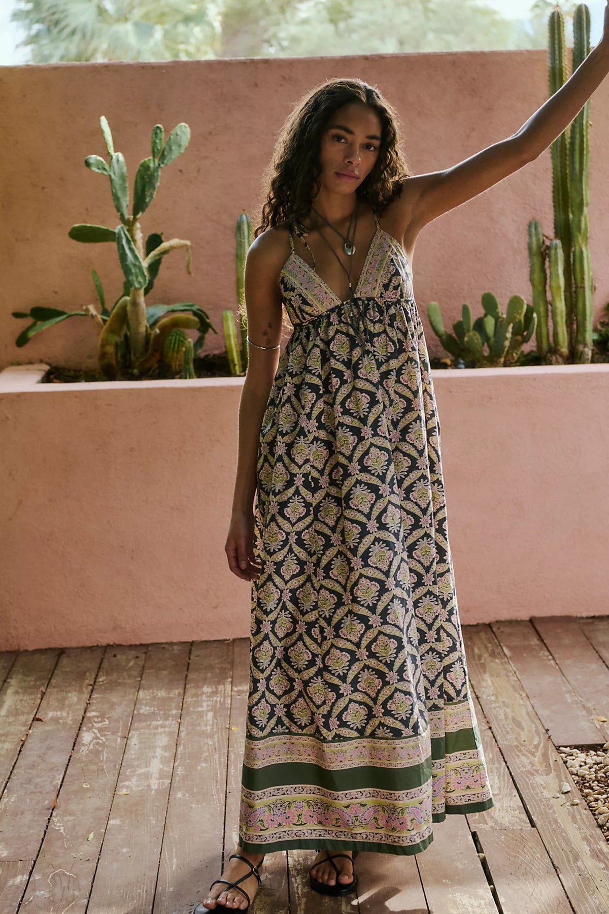 Woman in a patterned dress standing on a wooden deck with cacti in the background