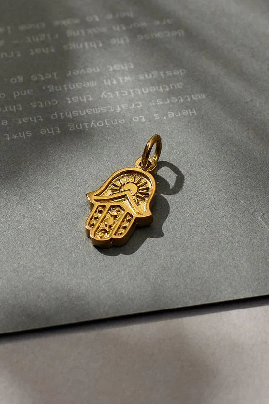 Gold Hamsa pendant on a textured gray surface