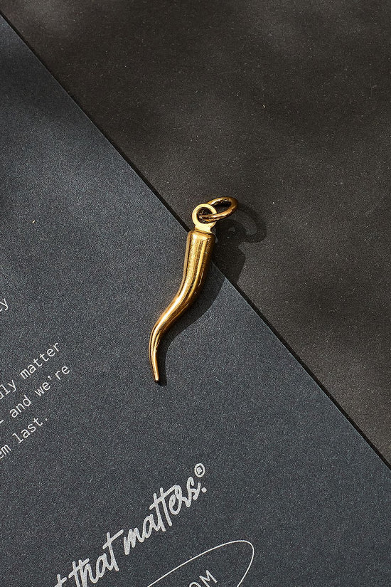 Gold necklace pendant on a black surface with 'it that matters' branding.
