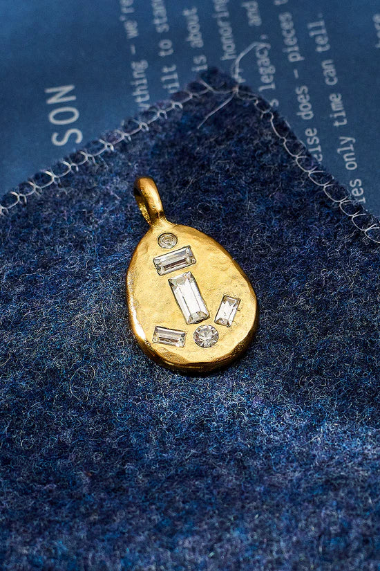 Gold pendant with embedded stones on a blue textured fabric background