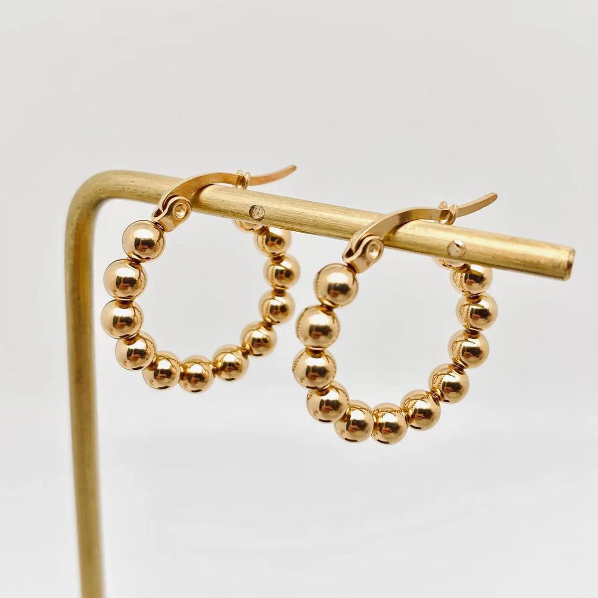 Pair of gold-plated stainless steel beaded hoop earrings on a display stand