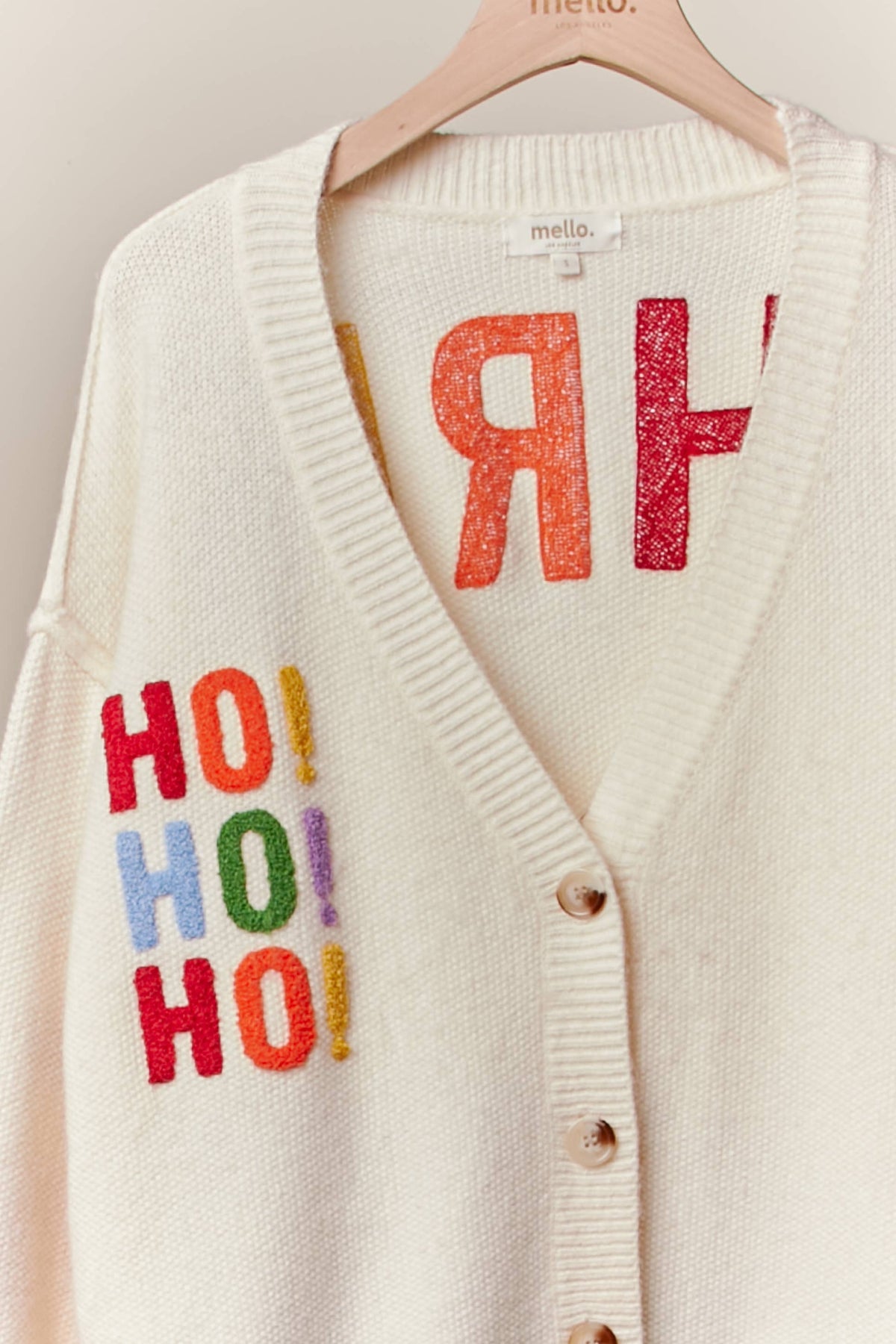 Close-up of the multicolor HO HO HO lettering on the front of the ivory V-neck cardigan
