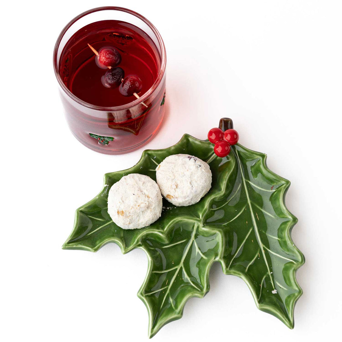 Holly sprig dessert plate with snowball cookies beside a glass of cranberry holiday cocktail