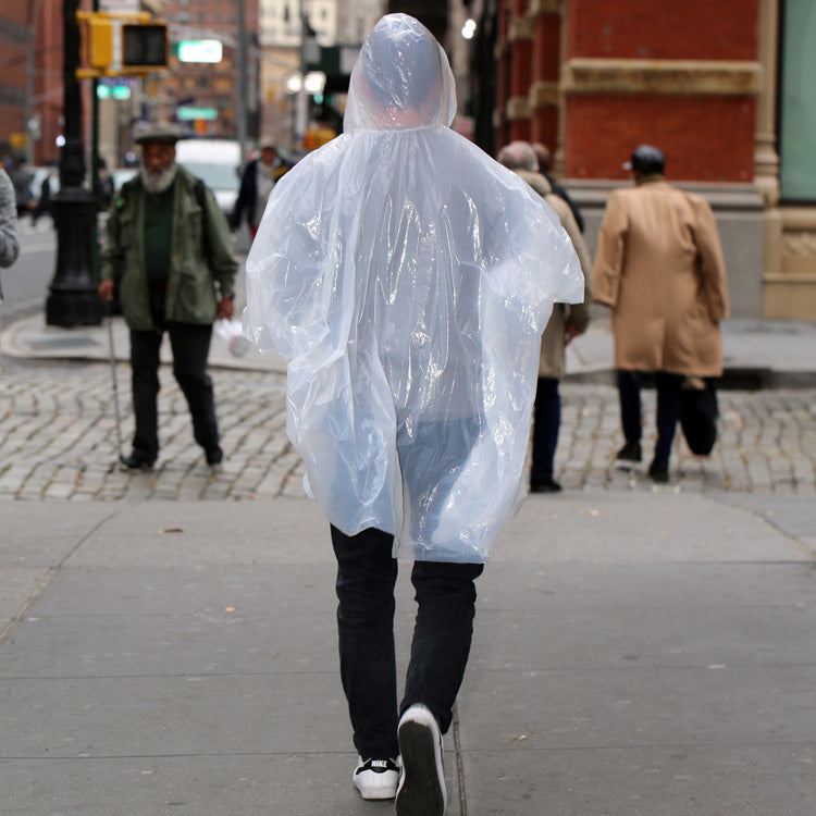 Person wearing a clear Kikkerland emergency rain poncho on a city street