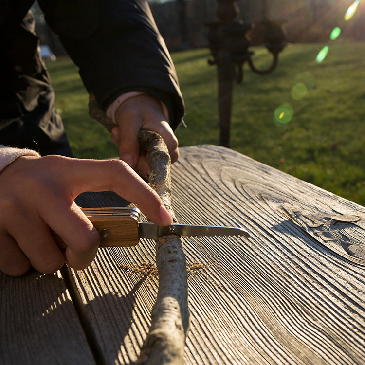 Whittling a stick outdoors with the Kikkerland Huckleberry pocket knife