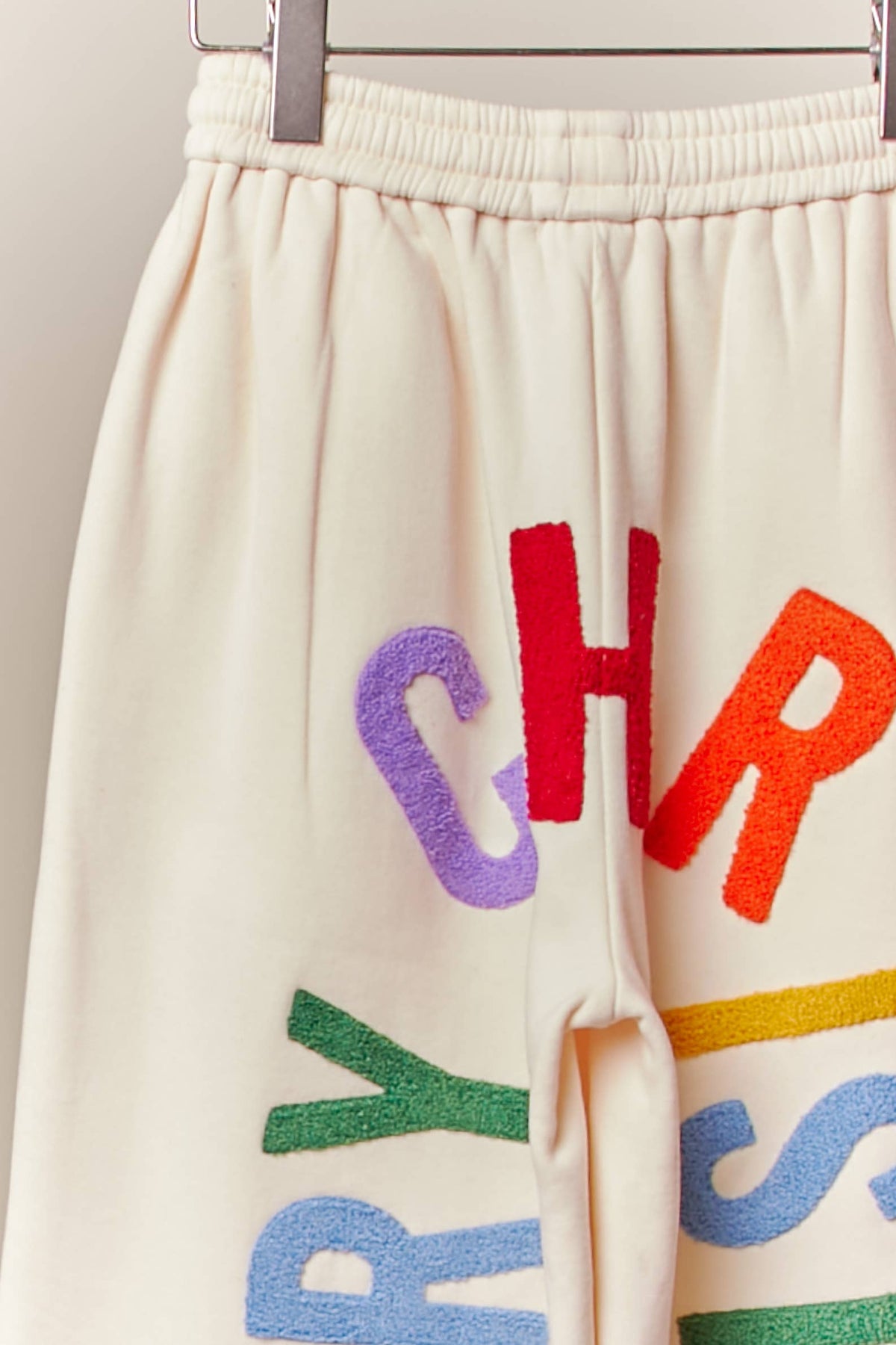 Close-up of the colorful textured Merry Christmas letters on the cream sweatpants