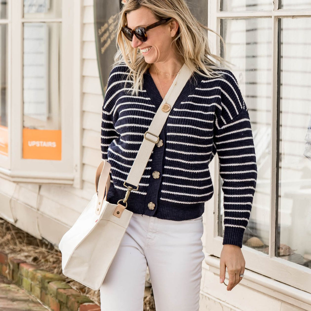 Woman wearing a navy striped cardigan and white pants, standing outdoors.