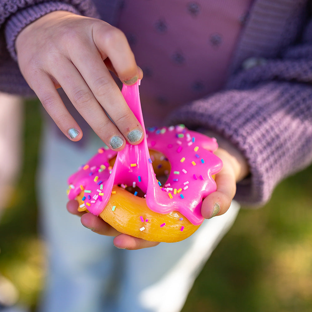 Child stretching the pink sprinkle donut Mushmeez taba squishy outdoors