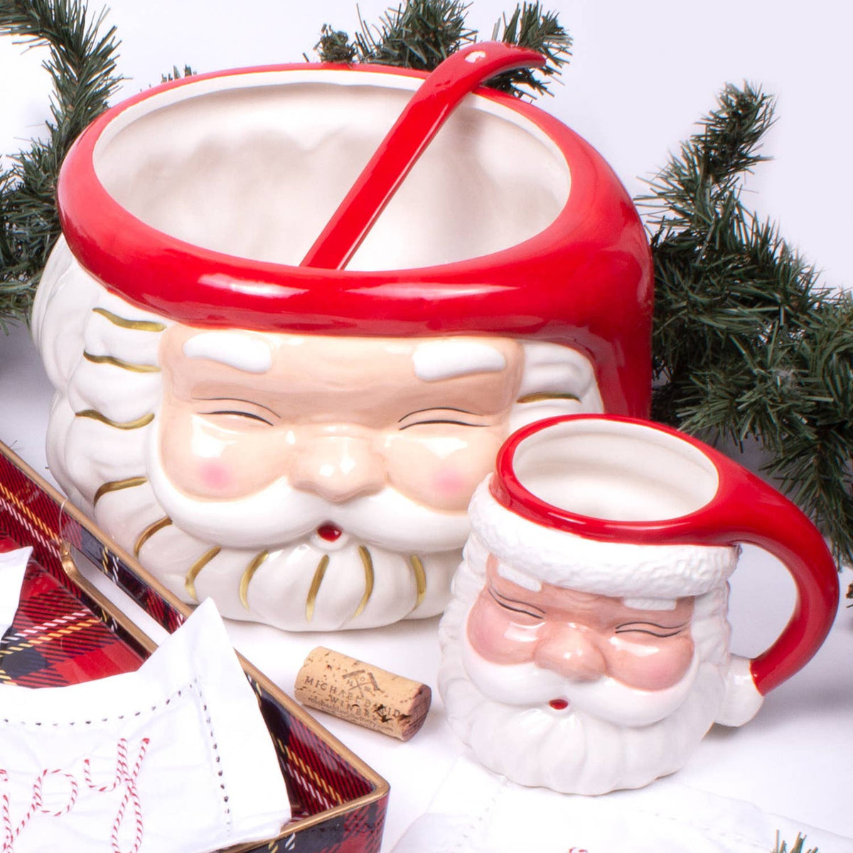 Red ceramic Santa coffee mug styled beside a large Santa serving bowl with evergreen branches