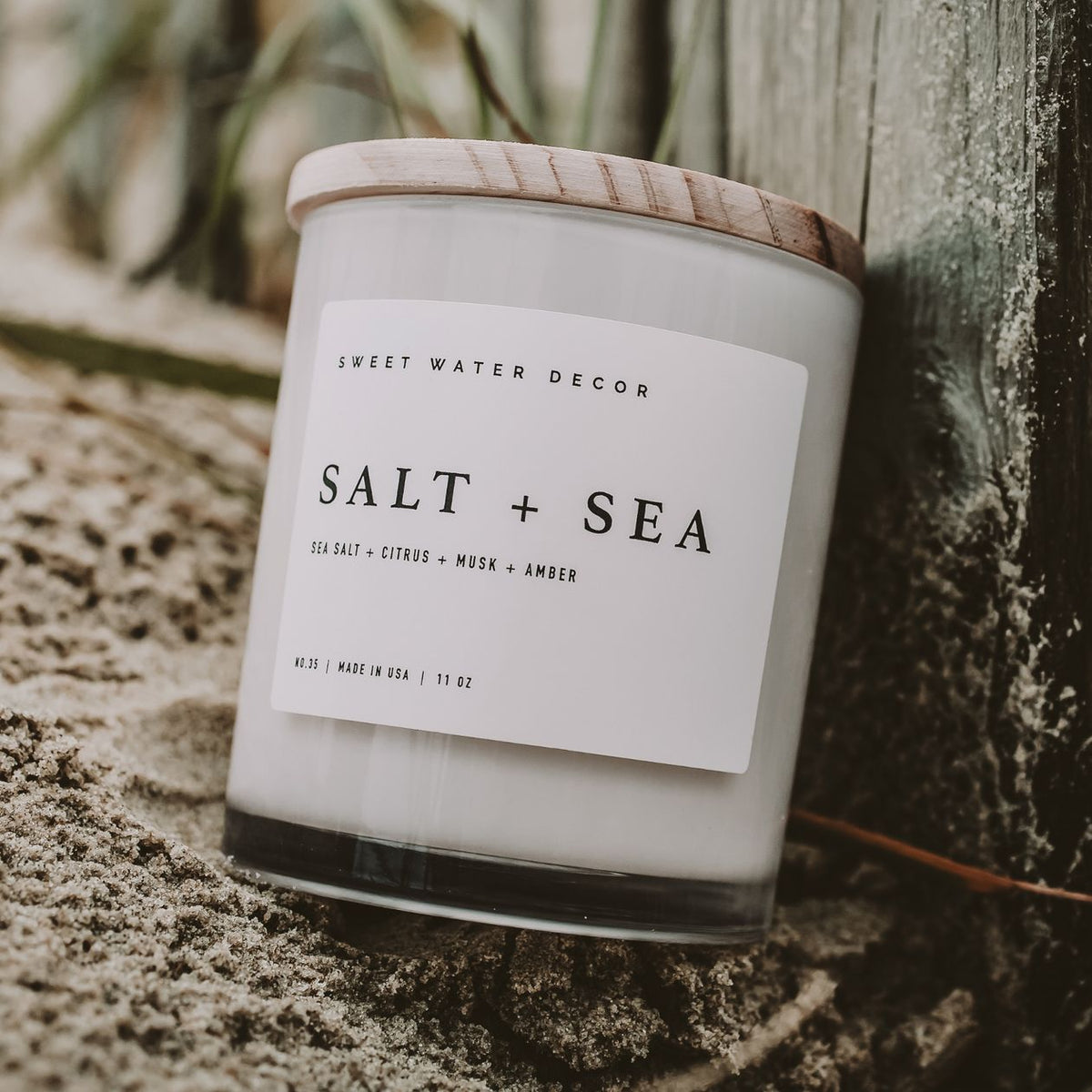 Candle labeled 'Salt + Sea' by Sweet Water Decor on a textured surface.