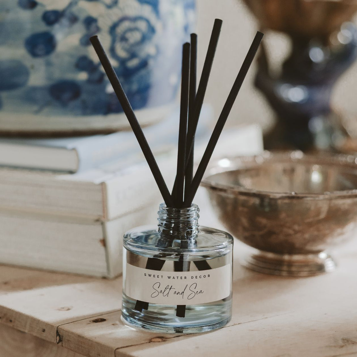 Reed diffuser with black sticks in a clear bottle on a wooden surface with decorative items in the background.