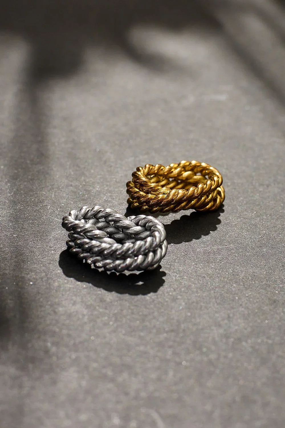 Two rings, one silver and one gold, on a textured surface.