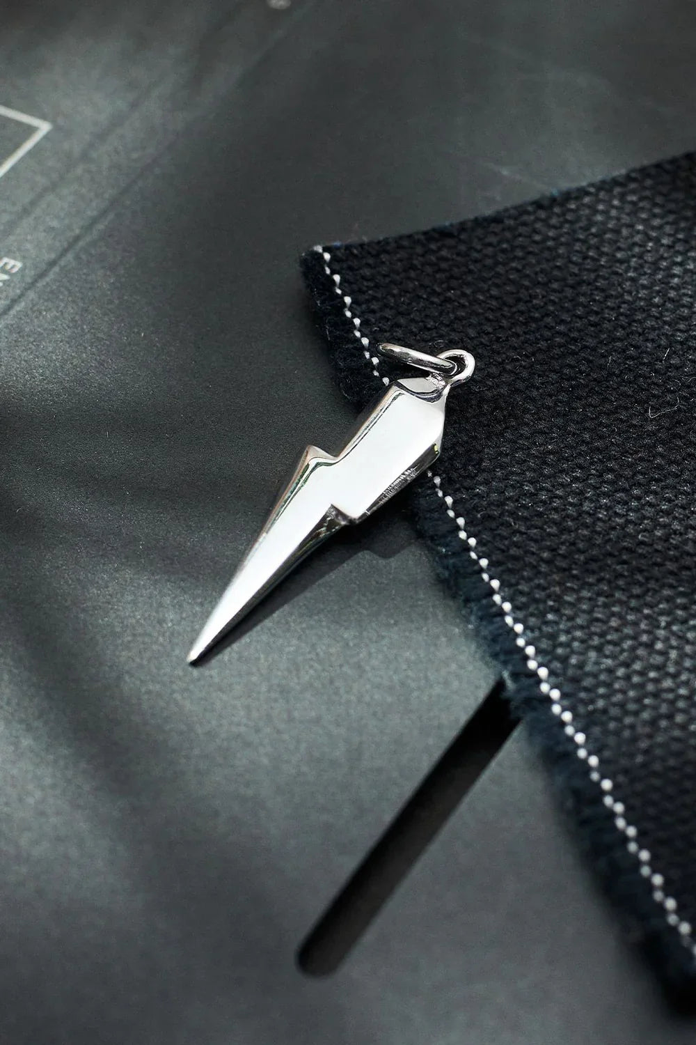 Silver lightning bolt pendant on a black textured surface