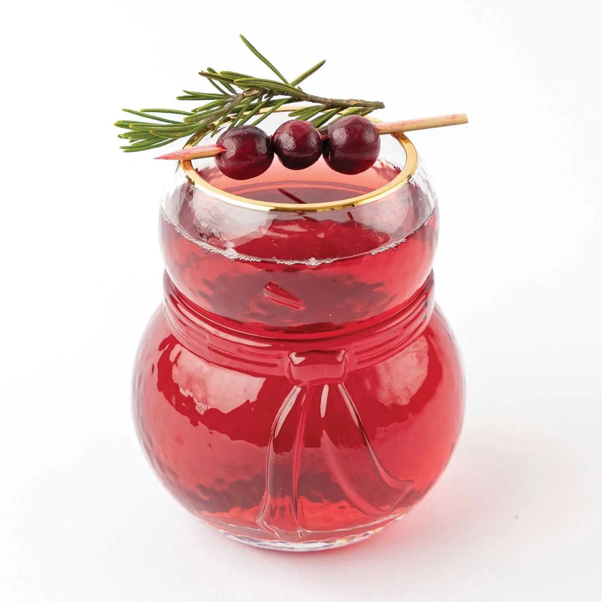 Snowman-shaped drinking glass with a gold rim filled with a red cranberry drink and garnished with cranberries and rosemary