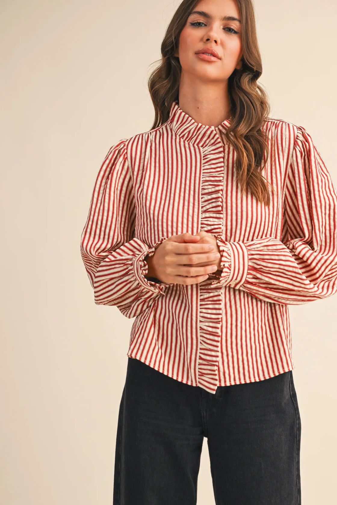 Woman wearing the &merci Striped Ruffle Blouse in red and cream stripes with a ruffled high neck and puff sleeves, front view