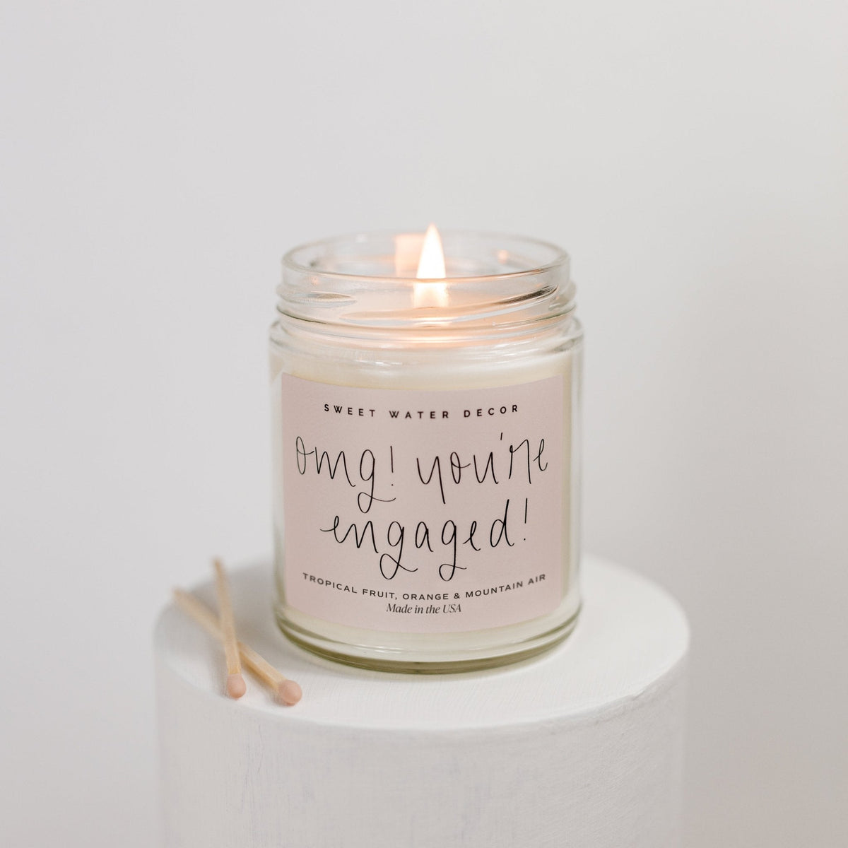 Lit Sweet Water Decor OMG You're Engaged soy candle in a clear glass jar on a white pedestal