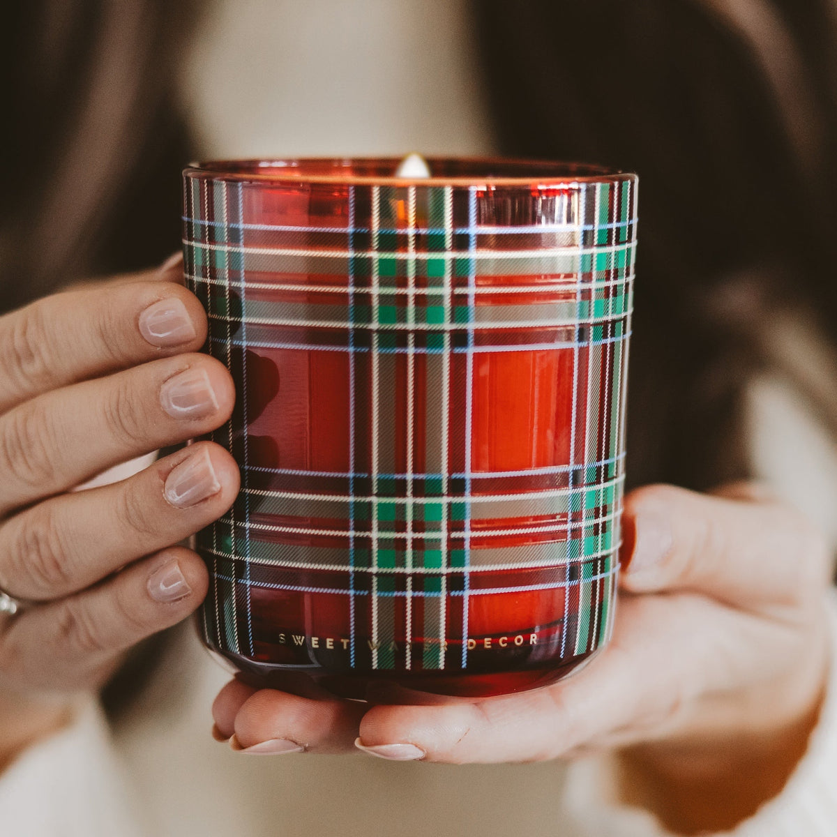 Hands holding the Warm and Cozy red plaid soy candle