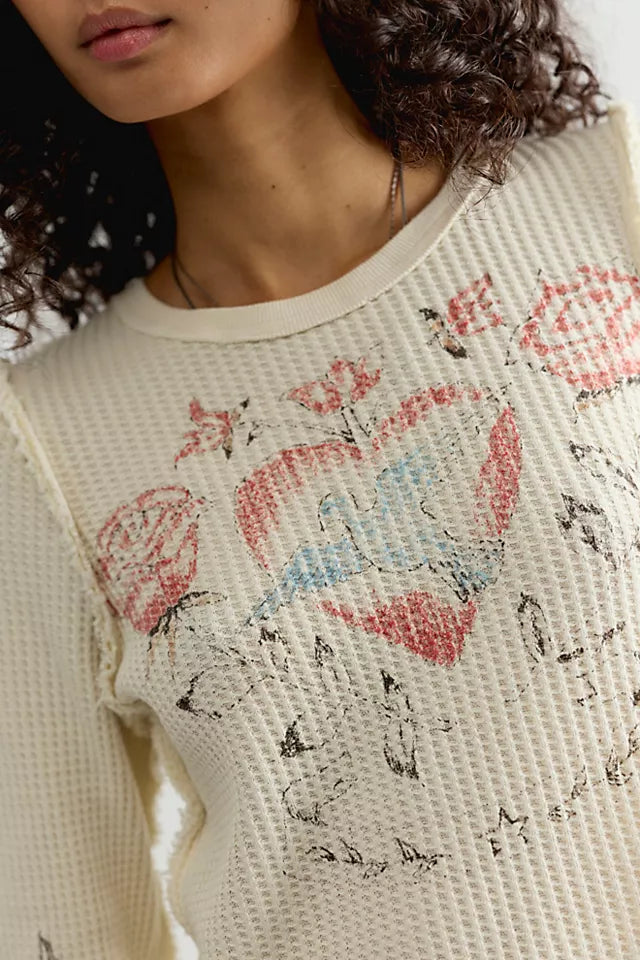 Close-up of a person wearing a cream-colored textured knit sweater with a distressed graphic print of red, pink, and blue hearts and black scribbles.