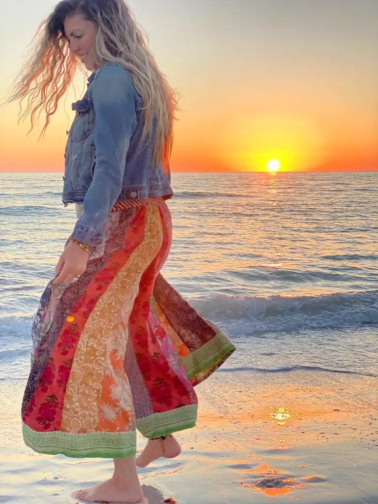 Woman in a colorful skirt standing on a beach at sunset.