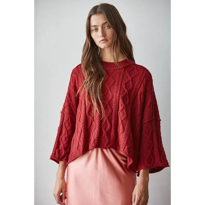Wine red cable-knit cotton pullover sweater with a boxy cropped fit and three-quarter sleeves, worn with a pink satin skirt
