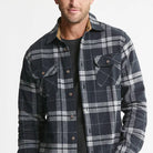 A man wearing a dark navy and gray plaid button-up flannel shirt over a black t-shirt, photographed against a clean white background.