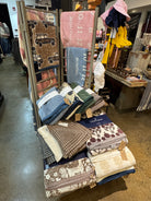 A retail display rack filled with folded and hanging baby blankets and swaddle blankets in various patterns and colors, including brown, pink, blue, green, and cream. The brand name 'Eagles Nest' is visible on several navy blue tags.