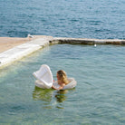 Woman holding a white inflatable chair in a pool with blue water.