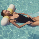 Woman in a black swimsuit lying on a yellow and white floatie in clear blue water.