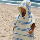 Child wearing a blue and white striped hooded towel on a beach