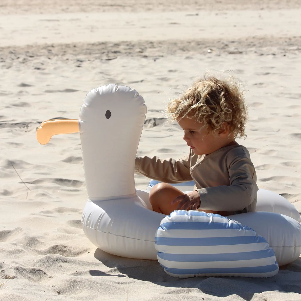 Child playing with an inflatable swan toy on a sandy beach