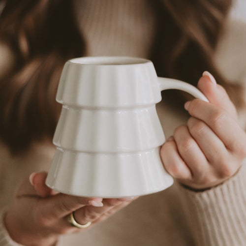Person holding a white ceramic mug with a textured design
