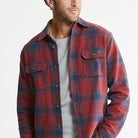 A man wearing a red and navy blue plaid flannel shirt over a gray crewneck t-shirt, photographed against a clean white background.