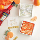 Aperol Spritz napkin tray styled with a bottle of Aperol, orange slices and spritz napkins