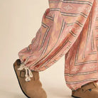 Close-up of the &merci Aztec Parachute Pants showing the drawcord toggle ankle cuffs in blush Aztec print