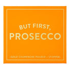 An orange square box with gold lettering that reads 'BUT FIRST, PROSECCO' and smaller text 'GOLD CHAMPAGNE POURER + STOPPER' at the bottom.