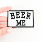 Patch with 'BEER ME' text held by a hand on a white background