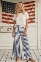 Woman wearing a white t-shirt and striped pants standing in front of an American flag.