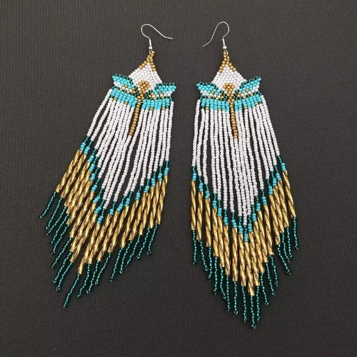A pair of long beaded dangle earrings with white, turquoise, and gold seed bead patterns on silver fishhook wires, displayed against a dark textured background.