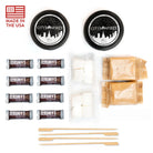 City of Fires marshmallow s'mores kit components laid out on a white background, including two black-labeled tins, Hershey's chocolate bars, marshmallows, peanut butter packets, wooden skewers, and a 'Made in the USA' flag graphic.