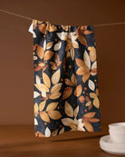Botanical Wonderland tea towel in navy with orange, tan, and cream autumn leaf print hanging on a line